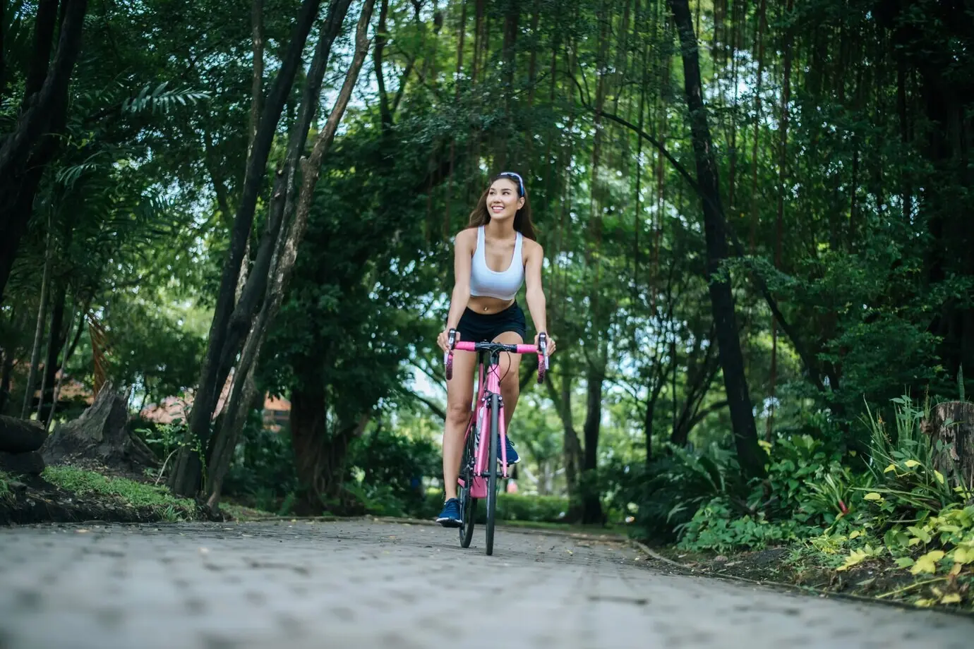 A woman cycling on a road bike in the park. A portrait of a young, beautiful woman on a pink bike.