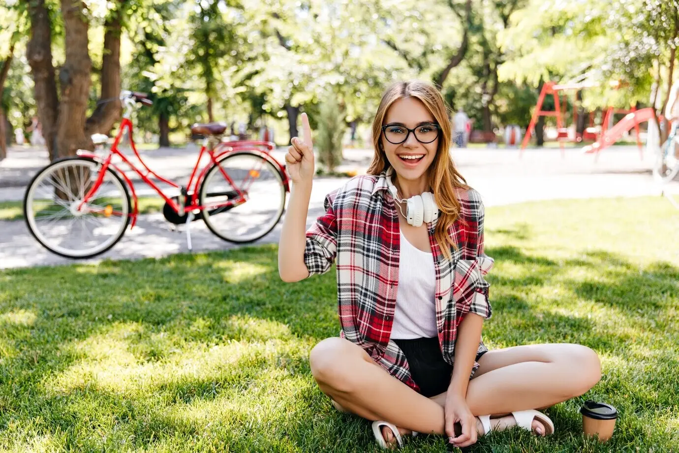 Cheerful young woman sitting on the grass with a genuine smile. An outdoor photo of a joyful Caucasian girl relaxing in the park.